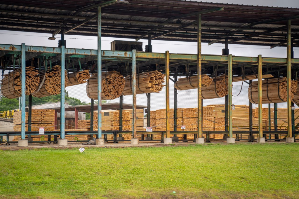 Image of stacked wooden planks in an outdoor lumber yard, showcasing industrial wood processing.